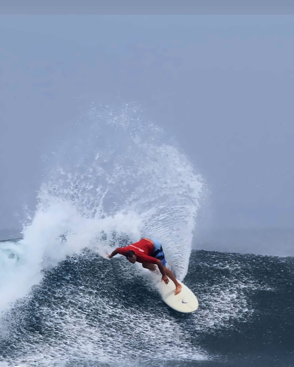 Deano in a red rash vest throwing a fan of spray off the lip of a wave at Ujung Bocur, Krui