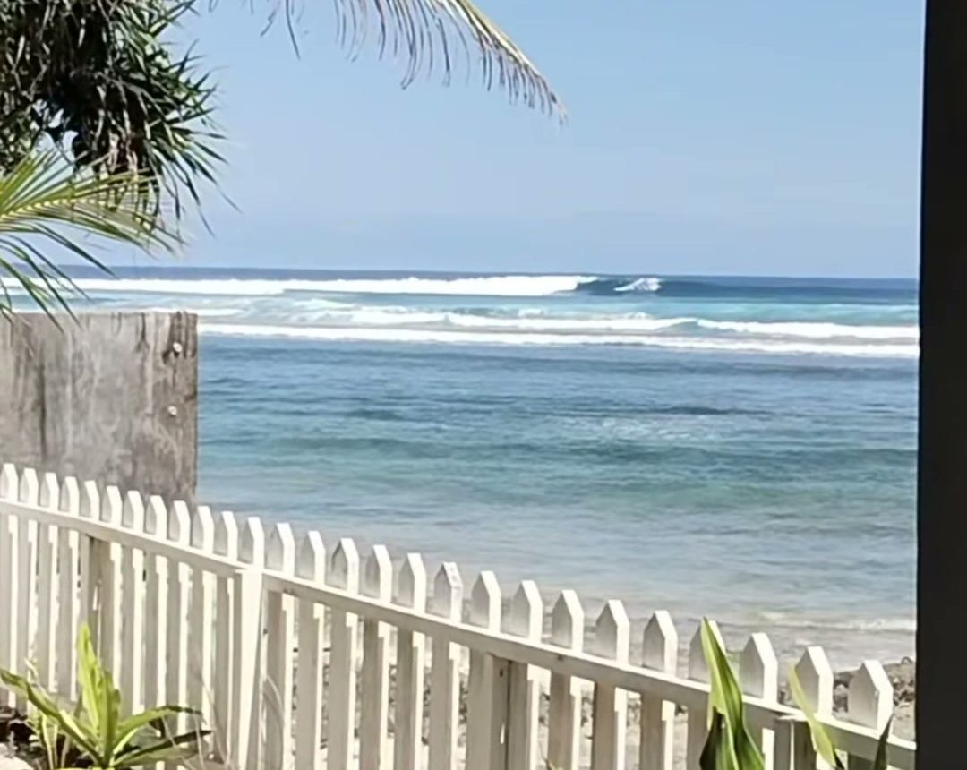 View over the white picket fence at Lani's to waves breaking on the Ujung Bocur reef, Tanjung Setia beach